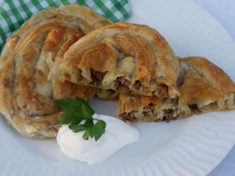 A plate with round pastries with meat and sour cream next to them.