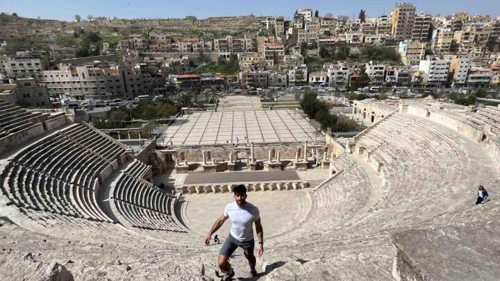 Stefan of Nomadic Boys standing on the steps of an amphitheater with a city in the background.