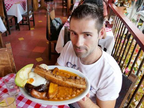 Seby from Nomadic Boys holding a plate of Bandeja Paisa in Colombia