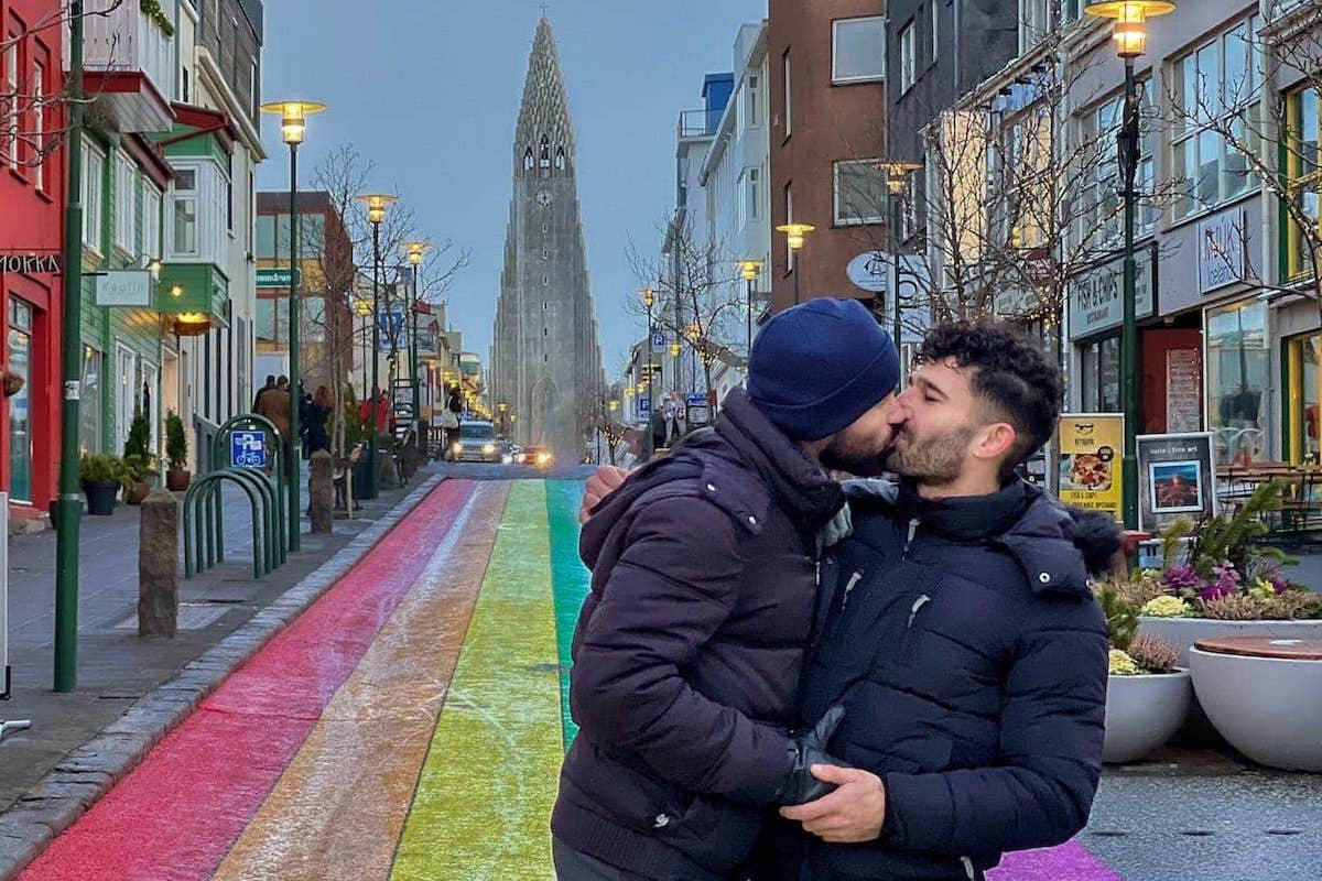 Gay couple kissing on Reykjavik's rainbow road with the Hallgrímskirkja Church in the backgorund.