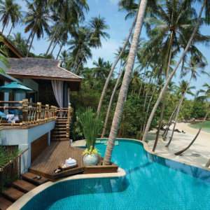 A villa with a private swimming pool next to a beach with palm trees surrounding.