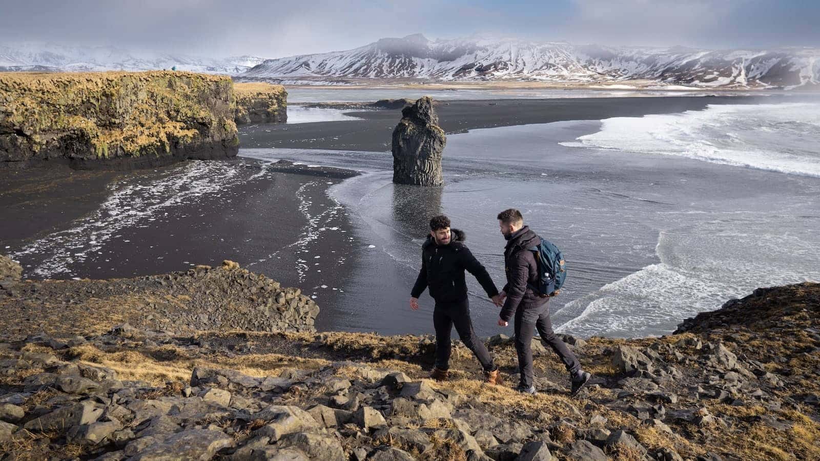 Gay couple holding hands and hiking in Dyrholaey in Iceland.