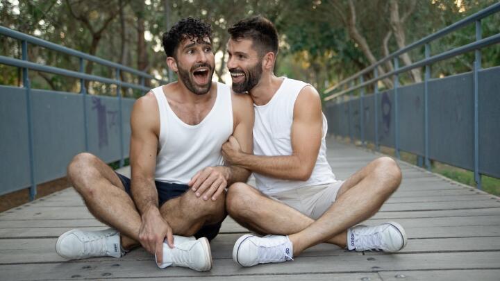 Gay couple Stefan and Seby sitting on the floor giggling together.