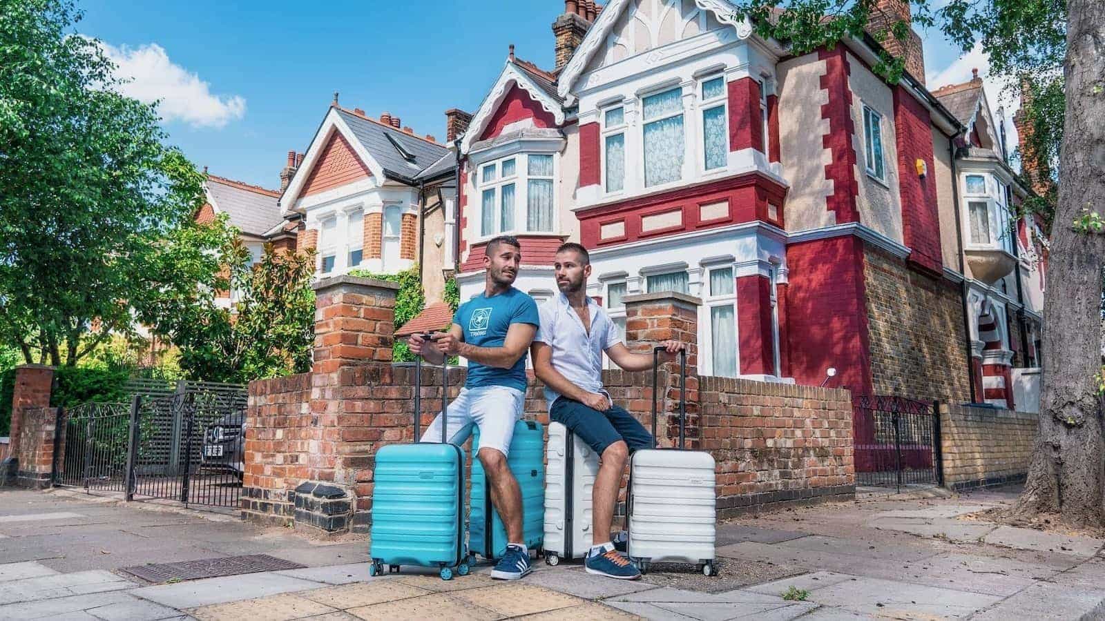 Gay couple Stefan and Seby sitting on their suitcases looking at each other.