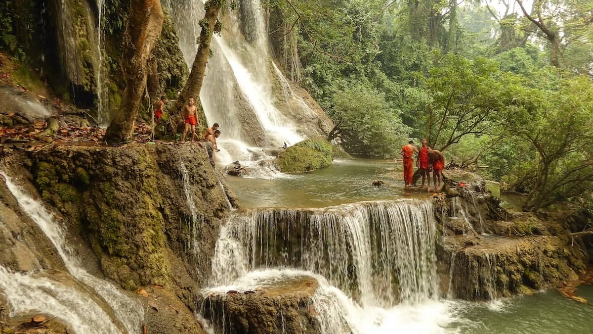 Gay couple at Kuang Si Falls in Luang Prabang in Laos with monk boys in red robes.