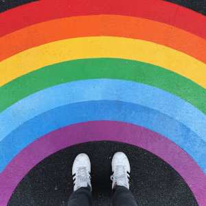 A painted rainbow on the ground as seen from someone looking down at their sneakers in front of it.