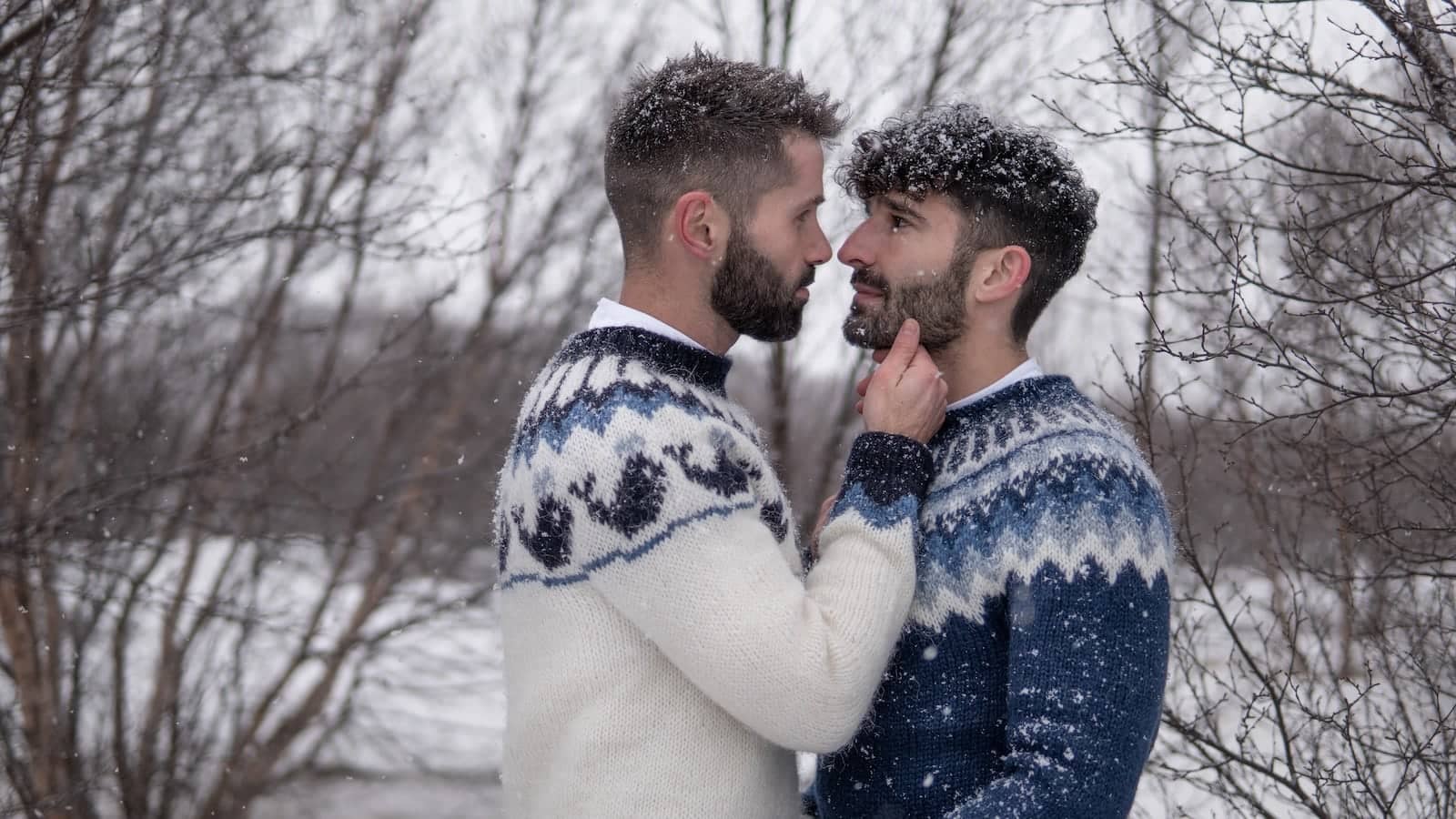 Gay couple wearing lopapeysas Icelandic wool jumpers at the Hraunfossar waterfall.