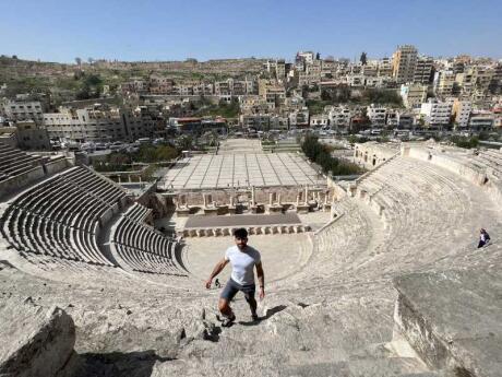 Stefan of Nomadic Boys standing on the steps of The Roman Theater in Amman with a view of the city in the background.