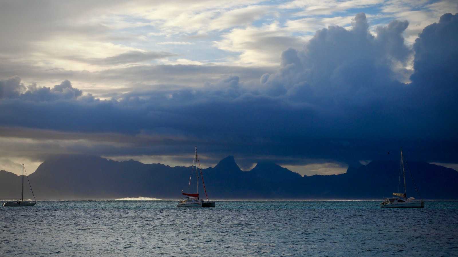 Three yachts on water with ominous clouds in the background.