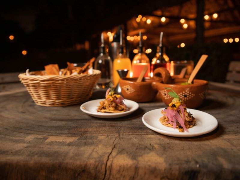 A rustic wooden table at The Traveler's Table in Playa Del Carmen with tacos and drinks.