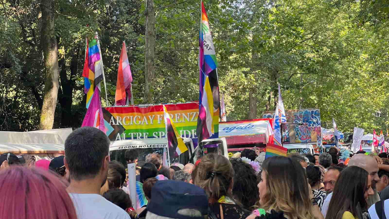 People walking with rainbow flags down a tree-lined road at Toscana Pride in Florence.